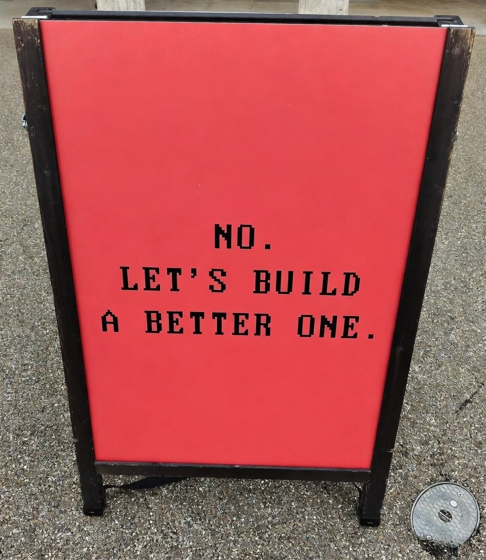 Red pavement sign with the words, No. Let's build a better one.
