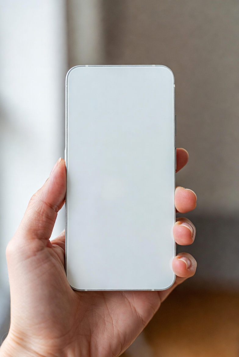 Hand holding a phone-shaped device with a blank white front and no visible screen interface.