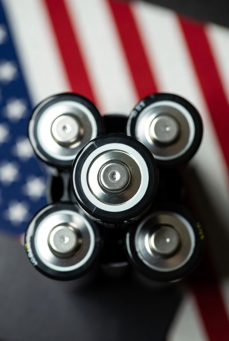Five cylindrical batteries arranged over a blurred United States flag.